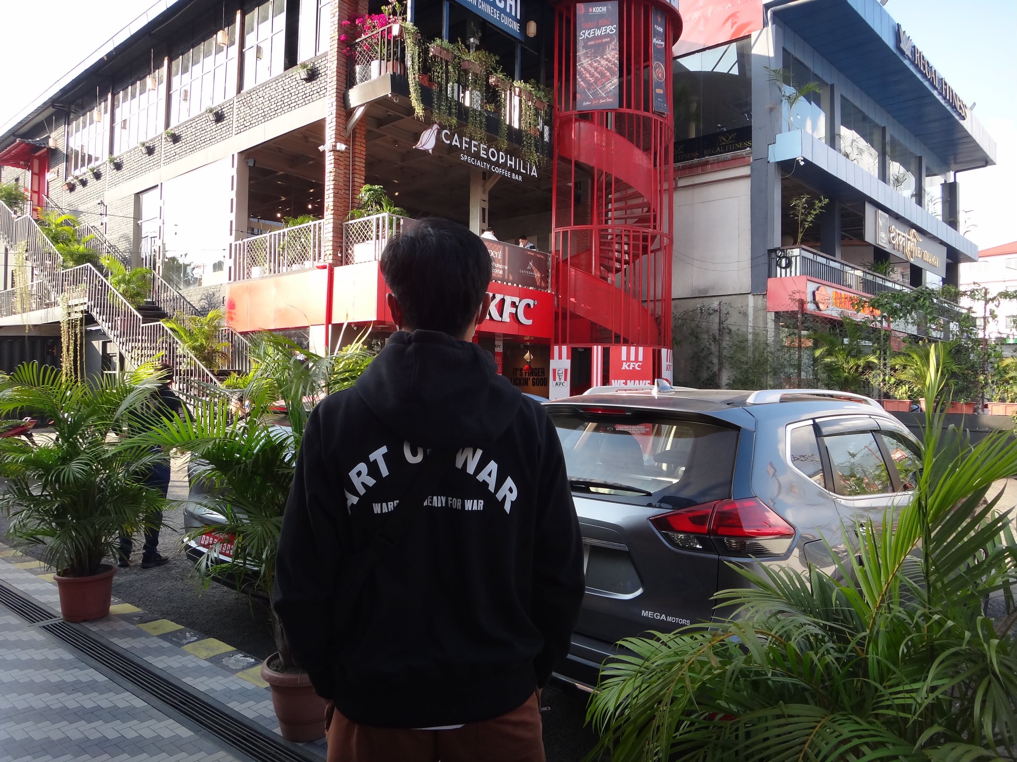 Back of a black KOA hoodie with the “Art of War — Warriors ready for war” print, worn on a street in Kathmandu
