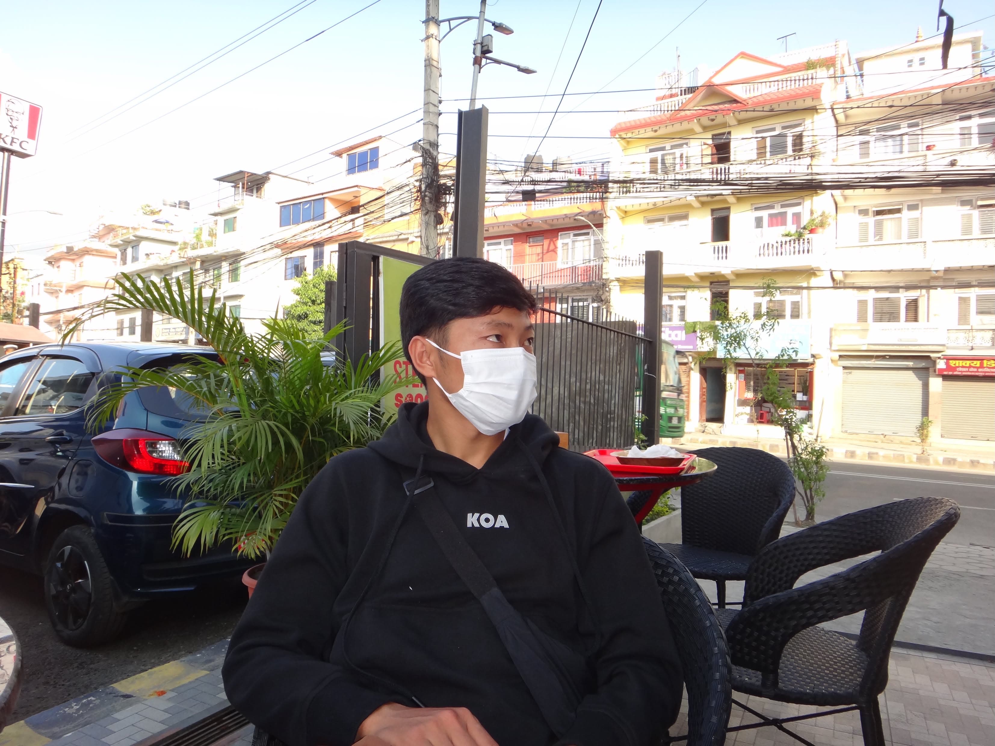 Man in a black KOA logo hoodie sitting at a street café in Kathmandu